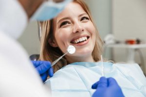 A female patient is sitting in a dentist's chair with a smile, displaying her shiny white teeth.